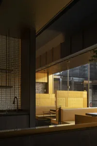 Dining area with tables, chairs, and a bar, surrounded by gold tile walls, potted plants, and a sophisticated atmosphere