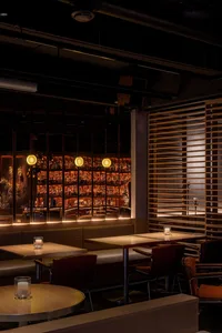 Modern bar area with a long counter and chairs, surrounded by dining tables, with warm and inviting lighting