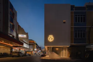A nighttime photo of a white building with a yellow neon sign, surrounded by parked cars and motorcycles in a lively urban environment