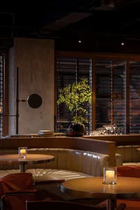 Warm and inviting restaurant interior with wooden floors and walls, featuring tables, chairs, and a potted plant, with wine glasses on some tables