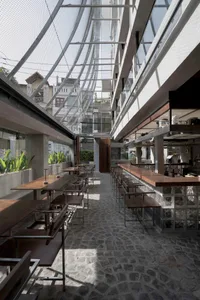 Open restaurant interior with modern design, clean lines, and minimalistic decoration, featuring multiple tables, chairs, and potted plants