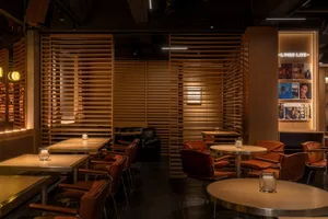 Warm and inviting restaurant interior with wooden walls and floors, featuring multiple dining tables and chairs, a bar, and ample seating options