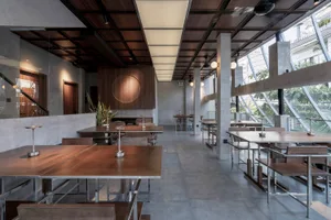 A modern restaurant with a large dining area, multiple tables, chairs, and potted plants, creating a clean and inviting atmosphere