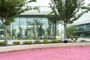 A modern indoor space with large windows, wood, and glass elements, featuring a relaxed and social atmosphere with people sitting and standing