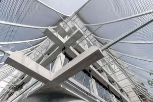 A modern building with multiple levels, stairs, and balconies, featuring concrete and glass construction, neutral tones, and natural lighting