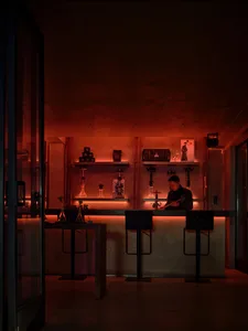 Dimly lit bar area with a stone-like wall, a counter, and stools, featuring bottles and a modern ambiance