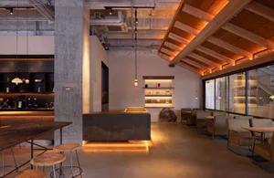Open modern living space with a grey countertop island, concrete walls, wooden elements, chairs, and a dining table, with a bright and inviting atmosphere
