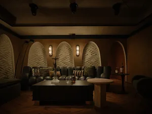 Cozy living space with a large couch, chairs, a dining table, and decorative vases, set in a room with arches and a warm atmosphere