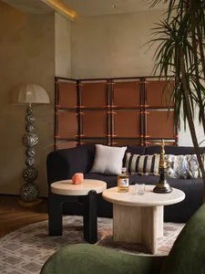 Cozy living area with a black couch, brown wooden panels, a dining table, and a potted plant, set in a warm and inviting atmosphere