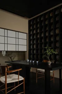 A modern dining space with a black table surrounded by chairs, decorated with bowls, cups, and vases, and well-lit for a comfortable atmosphere
