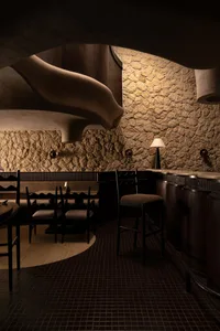 Cozy restaurant interior with a curved ceiling, stone walls, and dining tables, chairs, and bottles