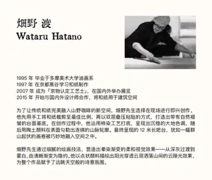 一位藝術家坐在地板上，周圍環繞書籍，在雜亂的工作室中創作一件藝術作品