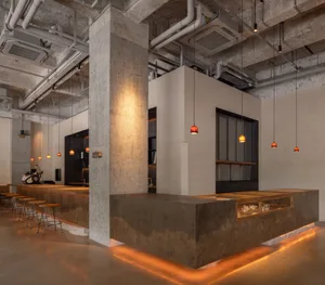Industrial open space with concrete walls and floors, featuring chairs and dining tables, with a modern and functional atmosphere