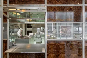 Industrial kitchen with two ovens, a sink, and three people in white uniforms preparing food in a professional and organized workspace