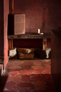 A rustic kitchen dining space with red walls, a tile floor, and a dining table with a chair, featuring two large rocks as design elements