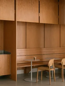 Warm and inviting restaurant interior with wooden walls and tables, featuring a cup on one table and empty chairs around two dining tables