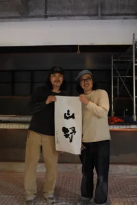 Two men posing with a black and white oriental-style painting, set against a neutral background
