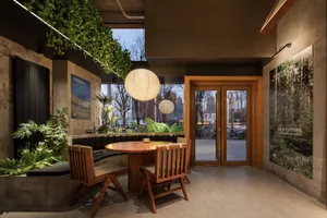 Warm and inviting restaurant interior with wooden floors and walls, featuring a dining table and chairs, and potted plants throughout