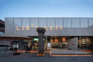 溫馨麵包店門面，配有玻璃窗、椅子、餐桌與盆栽，暖光照明