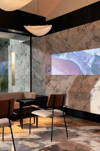 A modern interior design showroom with a marble wall, a large screen, two chairs, and a dining table, creating a sophisticated ambiance