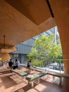 Dining area with wooden benches and tables, natural light from large windows, and several people enjoying meals in a warm and welcoming atmosphere