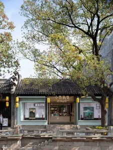 A traditional Asian-style building with stone walls, two storefronts, and window displays, surrounded by people and potted plants