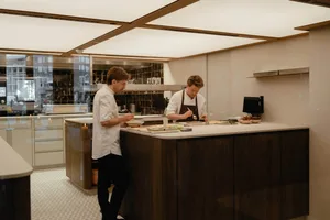 Two men preparing food together in a warm and inviting kitchen with wooden cabinets and countertops, surrounded by cooking utensils and cookbooks