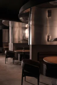 Empty modern restaurant with multiple dining tables and chairs, clean lines, and reflective surfaces on the walls