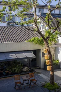 A gray-roofed Asian-style building with a patio area, chairs, and potted plants, blending traditional and modern architecture