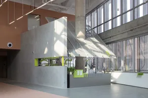 A modern lobby with a glass wall, potted plants, a bench, and chairs, creating a welcoming atmosphere with natural elements