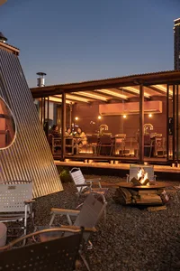 A restaurant patio with a dining table and chairs, a fire pit in the center, surrounded by a warm and inviting atmosphere