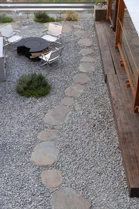 A stone walkway leads to a dining table surrounded by chairs in a relaxed outdoor seating area