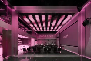 A modern interior design showroom with pink walls, various chairs, dining tables, and decorative bottles, set in a well-lit and inviting space