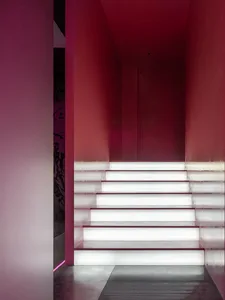 A grand staircase in a museum setting with marble steps, a red wall, and a sense of elegance