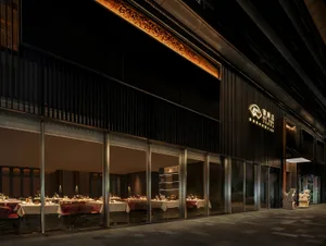 A modern Asian restaurant with a black exterior, featuring a spacious dining area with natural light, white tablecloths, and multiple tables arranged in various positions