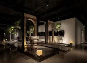 A calm and inviting art gallery space featuring a large stone sculpture, potted plants, and two vases, with a focus on the impressive stone centerpiece
