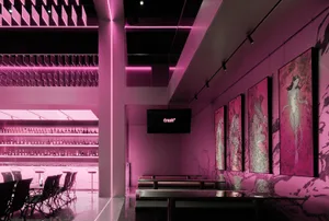 A modern bar area with a pinkish hue, featuring a large TV, chairs, and decorative bottles, creating a vibrant and inviting atmosphere
