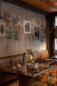 Casual restaurant interior with concrete walls, a bar, and dining table, featuring chairs and scattered bottles