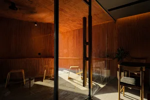 Warm and inviting living area with wooden floors and walls, featuring a dining table and two chairs, bathed in natural light