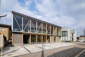A modern building with a large glass wall, wood accents, and potted plants, suggesting a sophisticated gathering or event space