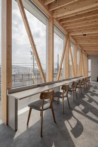 A dining area with multiple wooden chairs around a table, surrounded by a well-lit interior with a large window allowing natural light to enter