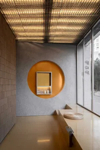 A modern bathroom with a circular mirror above a sink, a bench, and gray and orange walls creating a warm and contemporary atmosphere