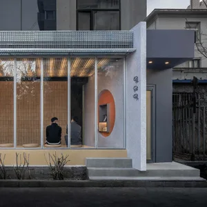 A modern building with a large window, featuring gray and yellow tones, with three people sitting in front of it, enjoying the view