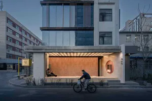 A serene urban scene with a building featuring a large window, a cyclist, and people sitting and standing nearby