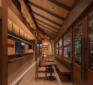 Warm and inviting restaurant interior with wooden floors, tables, chairs, and benches, featuring multiple bottles and ample seating options