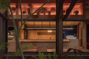Warm and inviting restaurant interior with a bar area, dining tables, and decorative elements like potted plants and vases