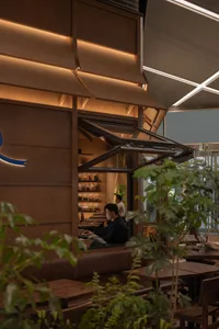 A casual indoor cafe with wooden furniture, people sitting and standing, and a relaxed atmosphere