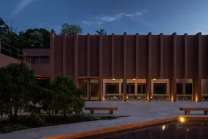 A brown building with multiple windows in various shapes and sizes, surrounded by outdoor benches