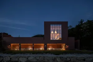 A modern building at night with a large window, stone and glass elements, and several chairs in a dining area or waiting lounge
