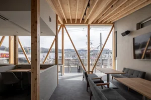 Cozy living space with wooden walls and floors, featuring a dining table, couch, bench, and two TVs